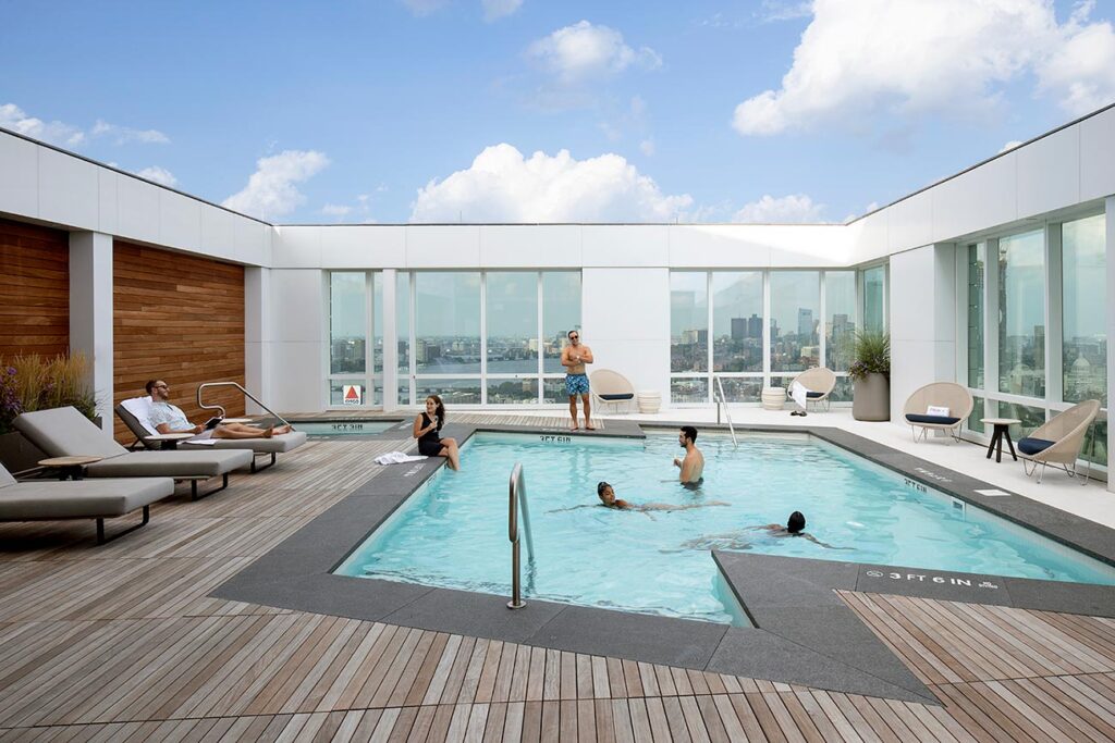 A rooftop pool with lounge chairs and a view of the city of Boston.